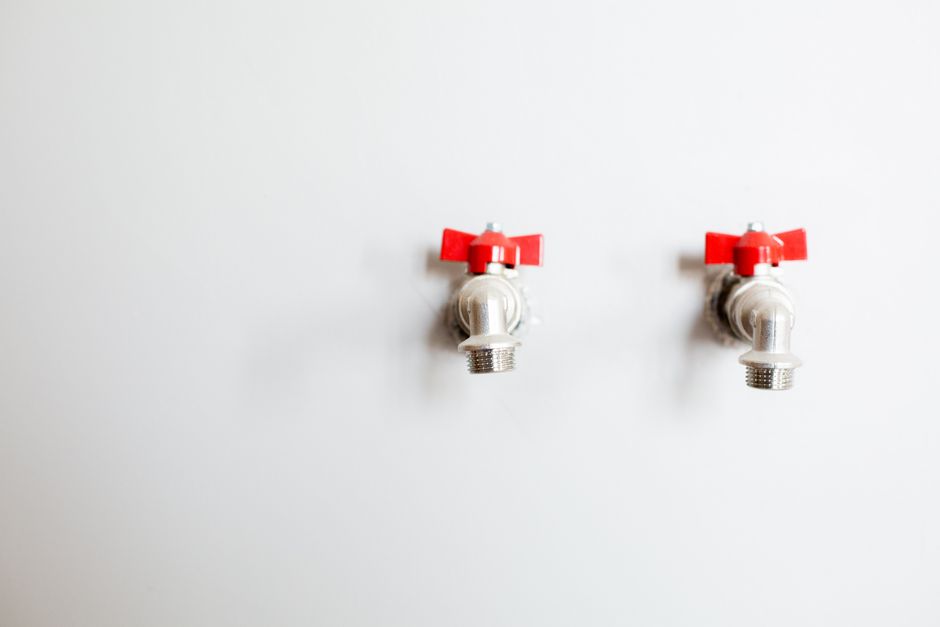 Close-up of two metal faucets with red handles against a white wall, showcasing plumbing detail.